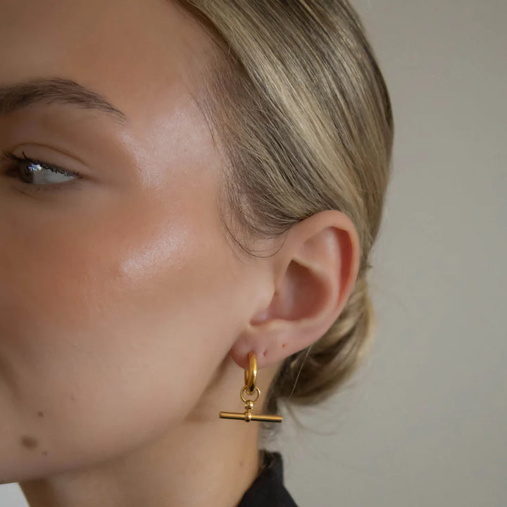 Close-up of a person wearing a gold hoop earring with a T-bar design.