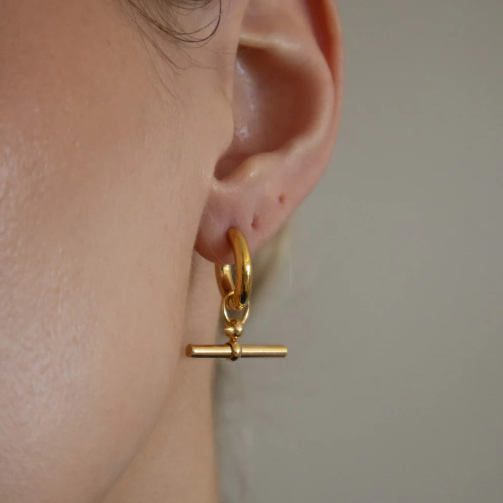 Gold earring worn on an ear with a neutral background