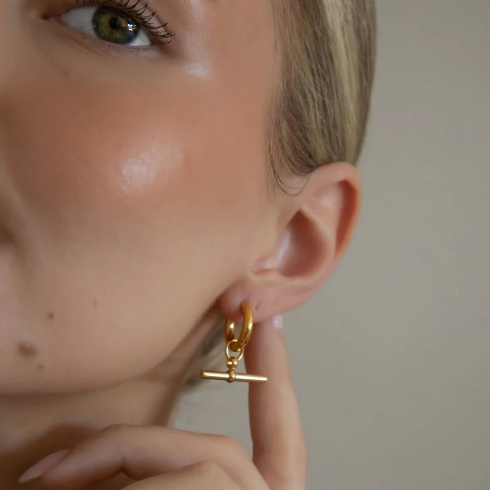 Close-up of a person wearing a gold earring with a T-bar design.