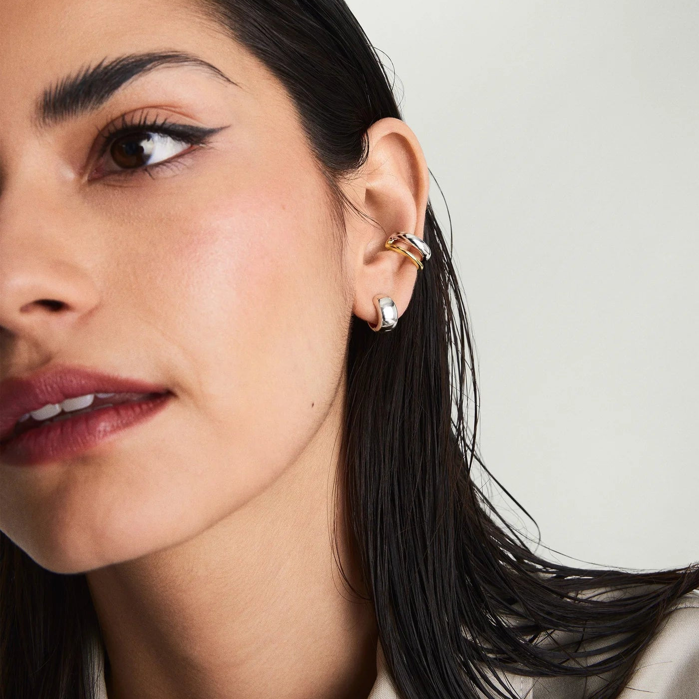 Close-up of a woman's ear with multiple earrings against a neutral background