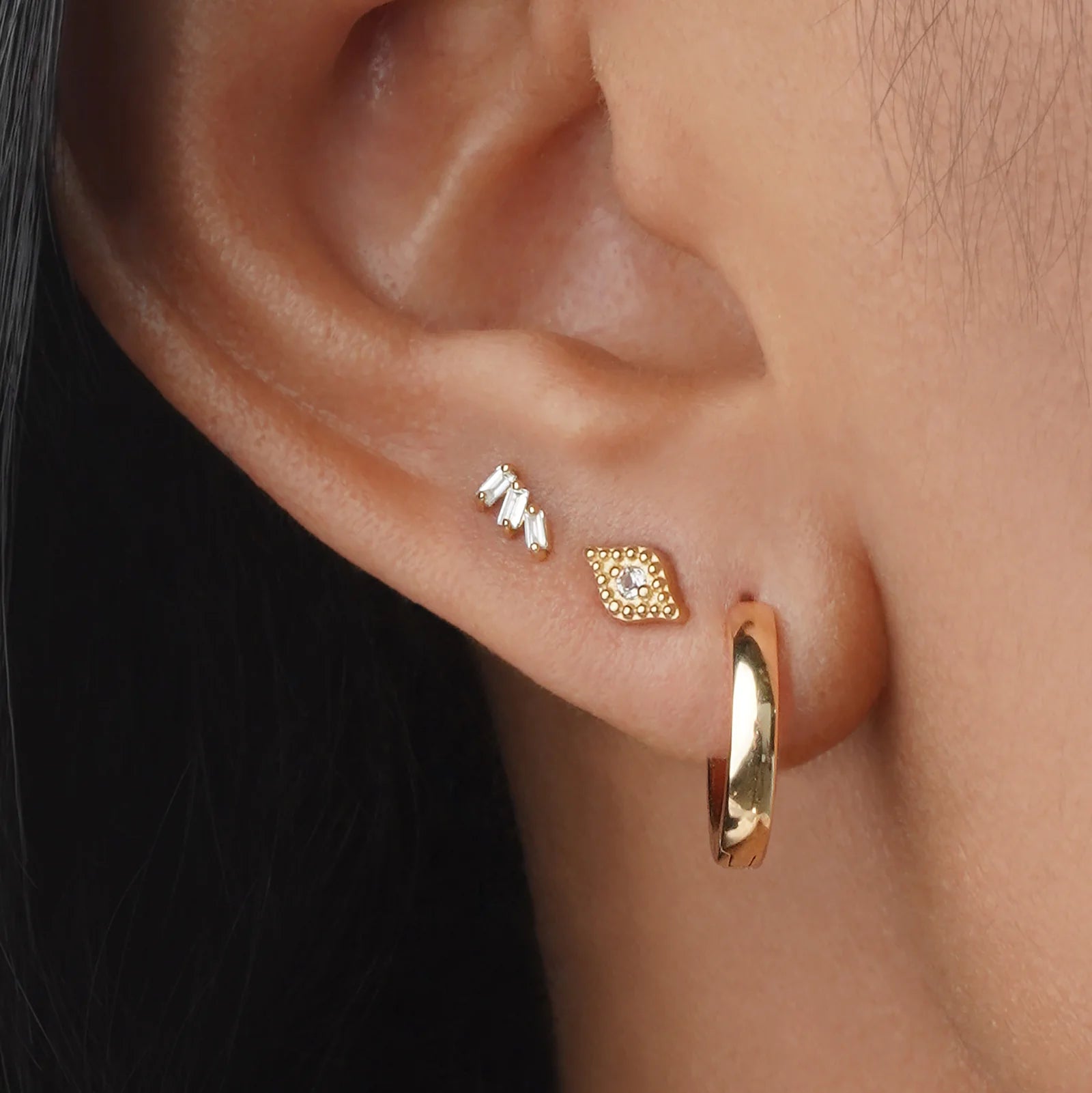Close-up of an ear wearing gold hoop earrings with a small diamond stud.