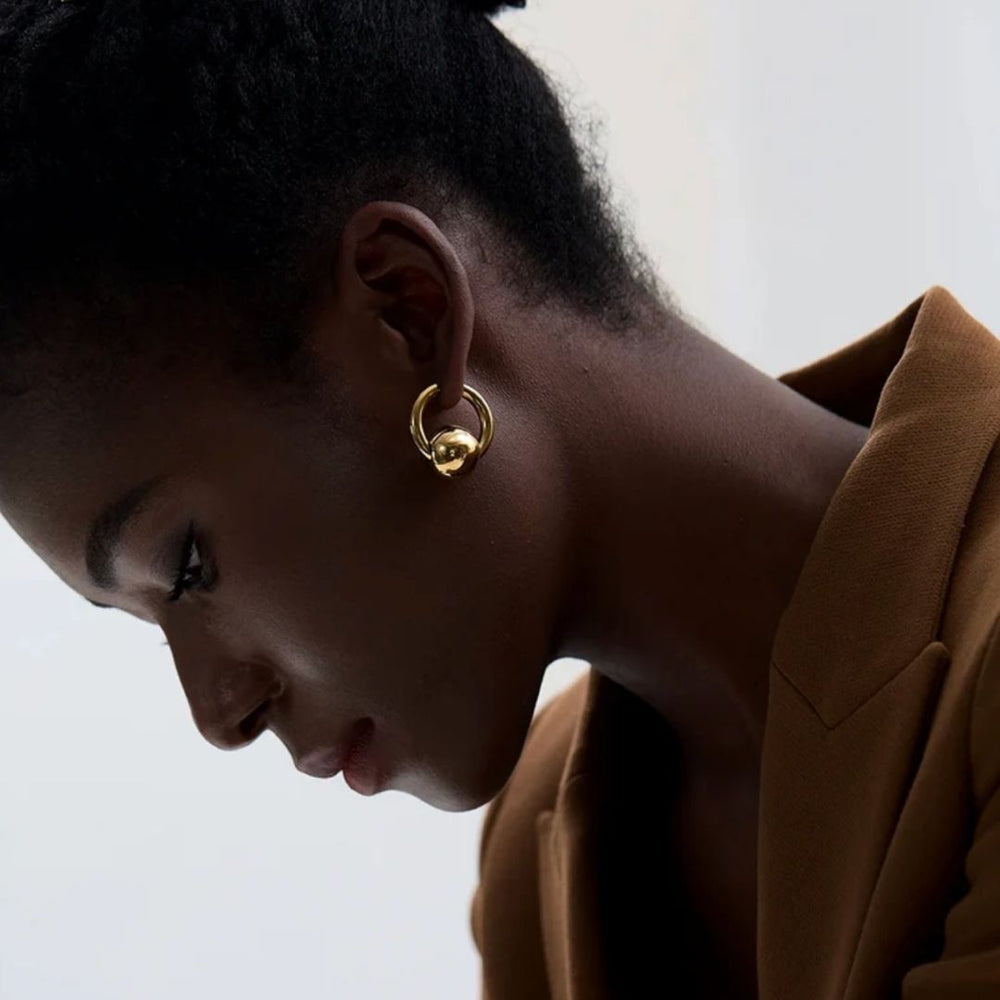 Close-up of a person wearing gold hoop earrings with a neutral background