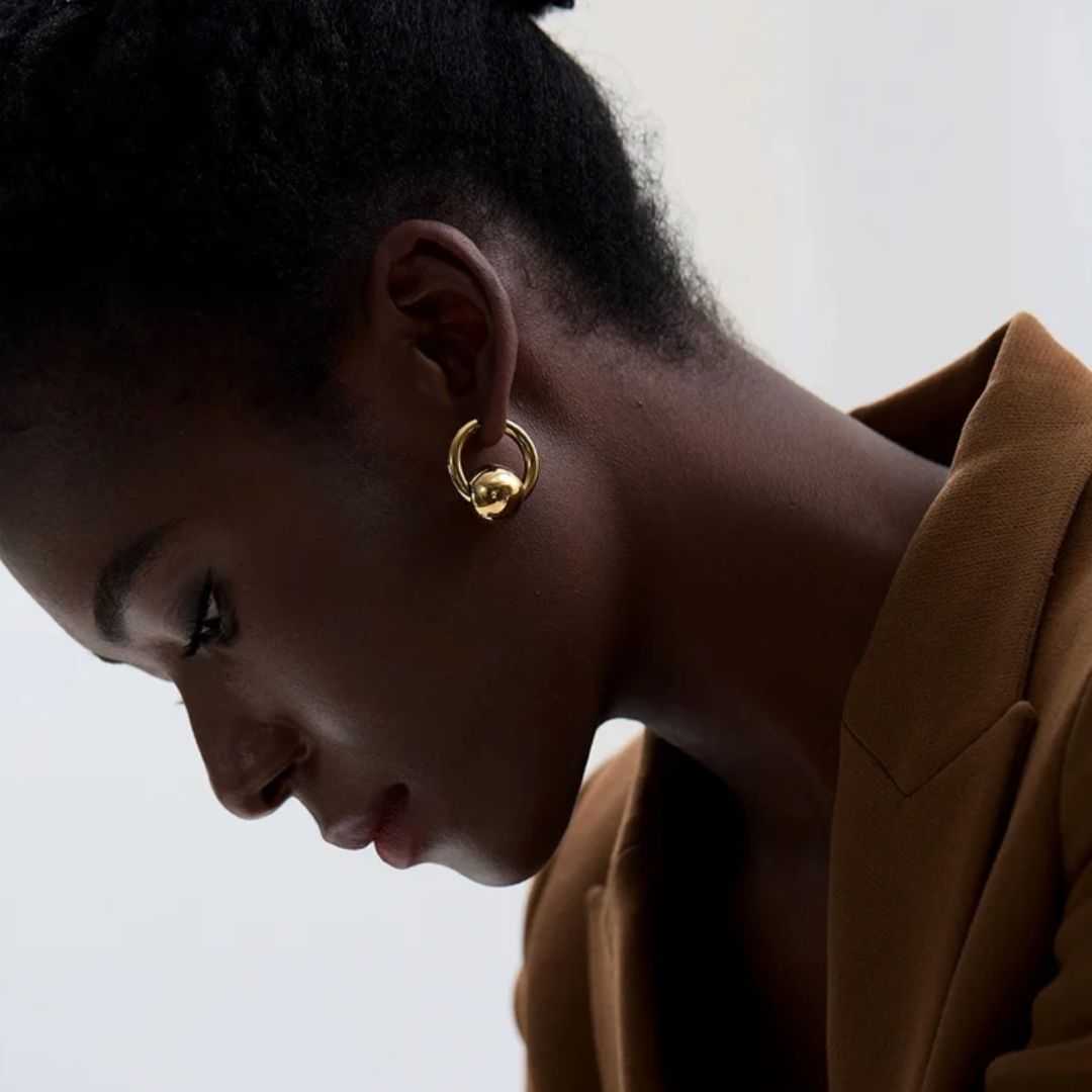 Close-up of a person wearing gold hoop earrings with a neutral background