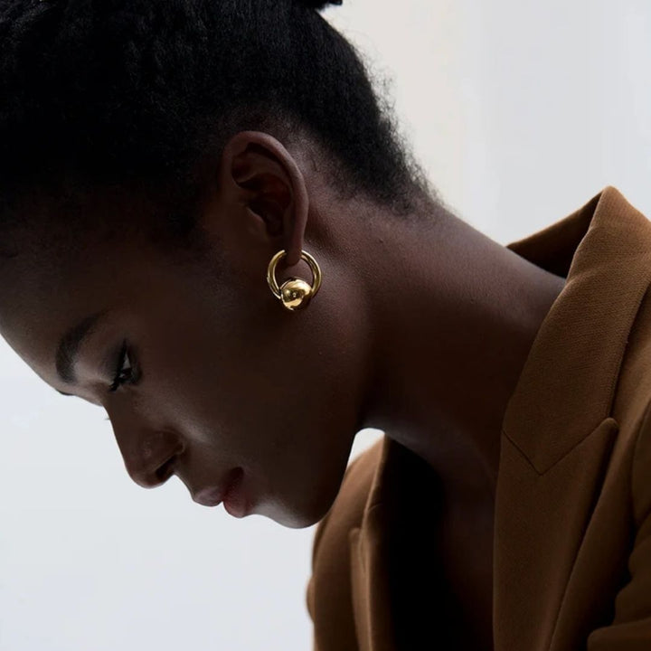 Close-up of a person wearing gold hoop earrings with a neutral background