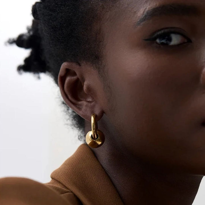Close-up of a person wearing a gold hoop earring with a blurred background