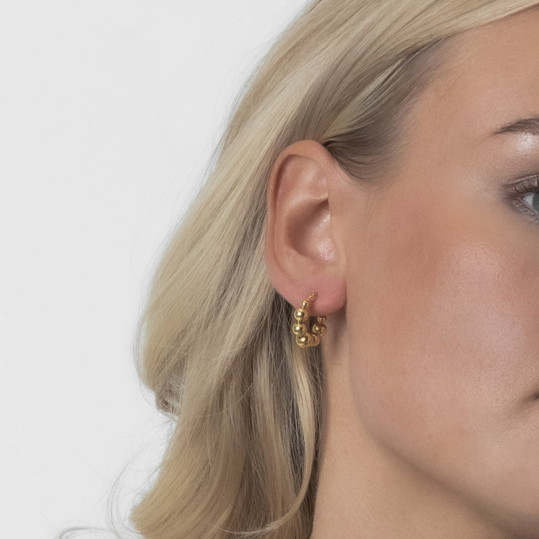 Close-up of a person wearing gold hoop earrings with a plain background