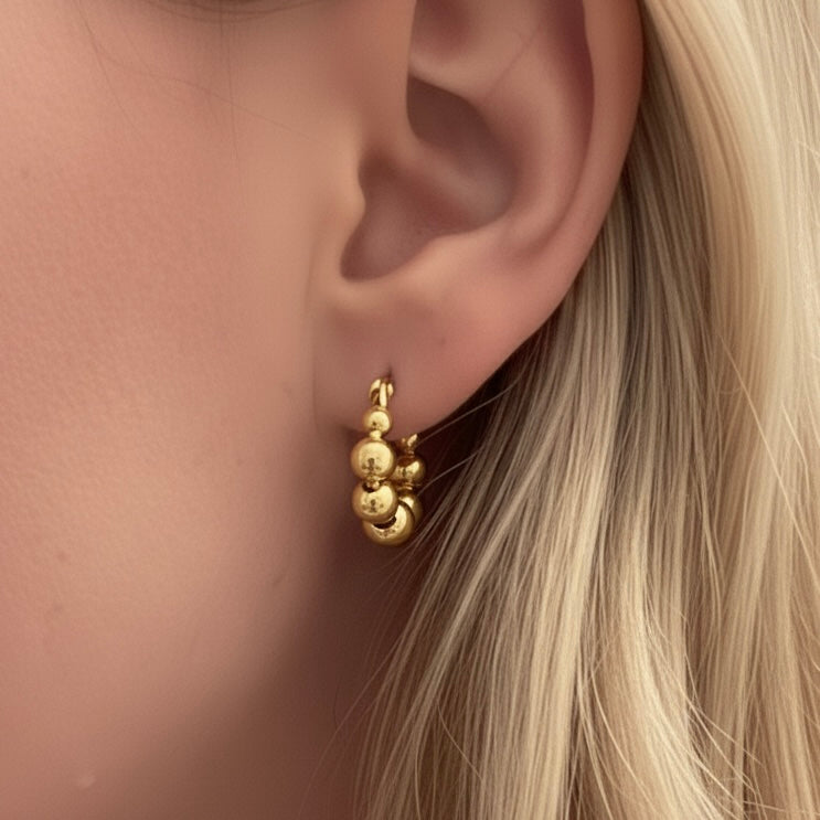 Close-up of an ear wearing a gold earring with blonde hair.