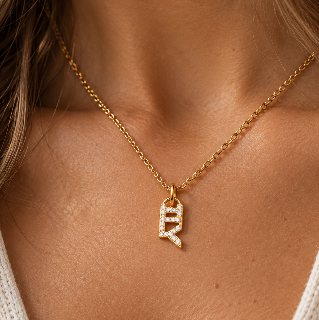 A close-up of a model wearing a delicate gold chain necklace with a letter ILY initial pendant encrusted with small clear stones.