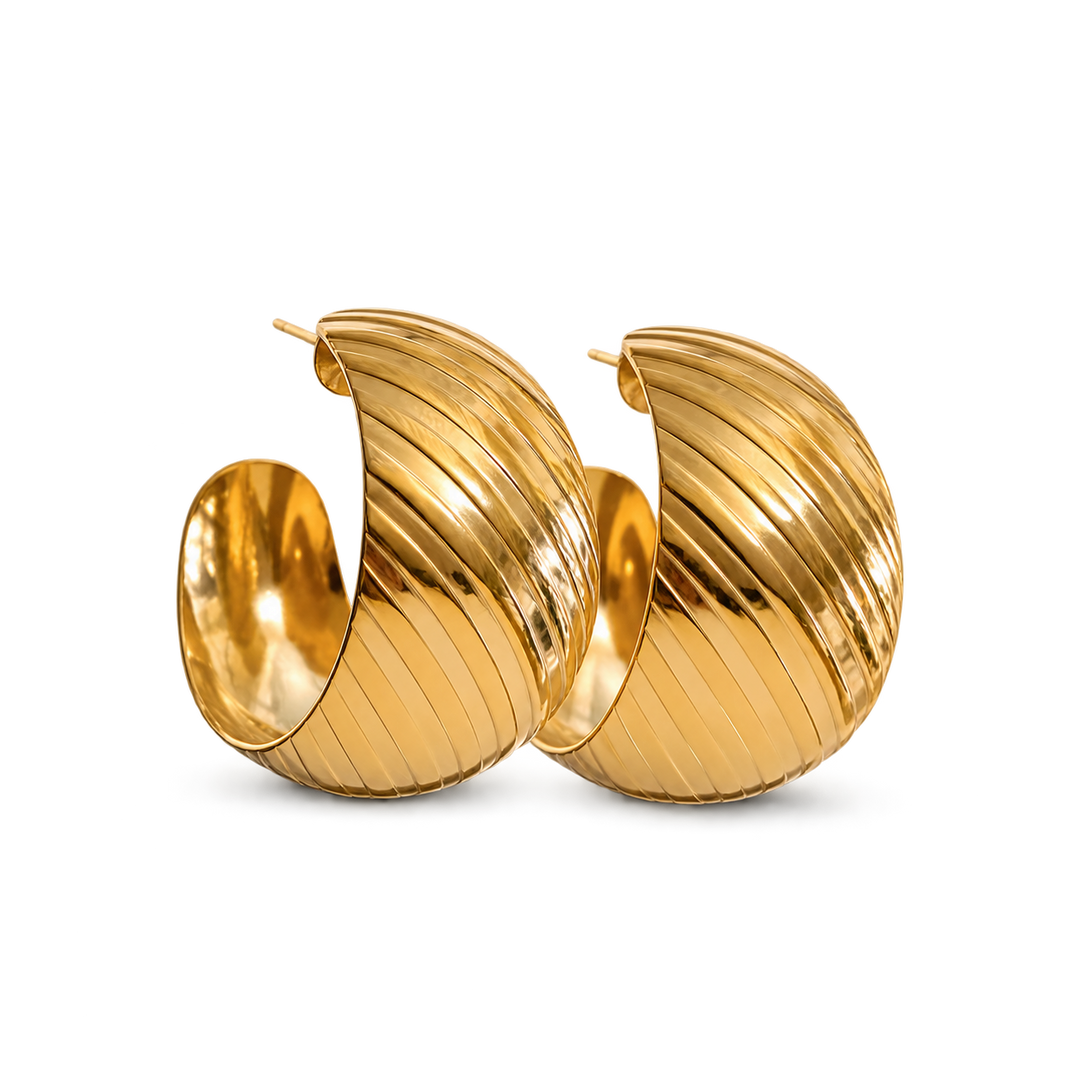 A pair of large, polished gold huggie hoop earrings with a distinctive ribbed, fluted texture, shown on a clean white background.