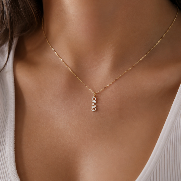 Gold necklace with 'LOVE' pendant on a person wearing a white top.