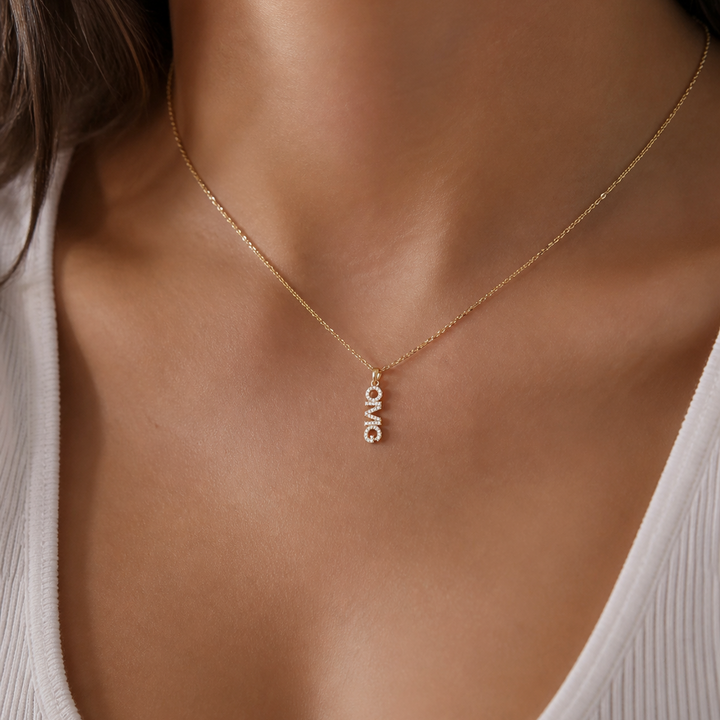 Gold necklace with 'LOVE' pendant on a person wearing a white top.