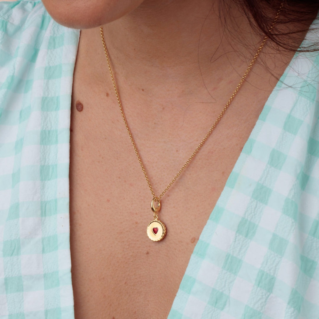Gold necklace with a heart pendant worn by a person in a light green checkered shirt.