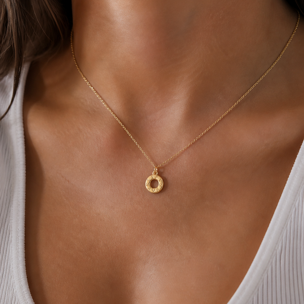 Gold necklace with a small pendant on a person wearing a white top.
