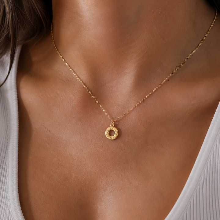Gold necklace with a small pendant on a person wearing a white top.