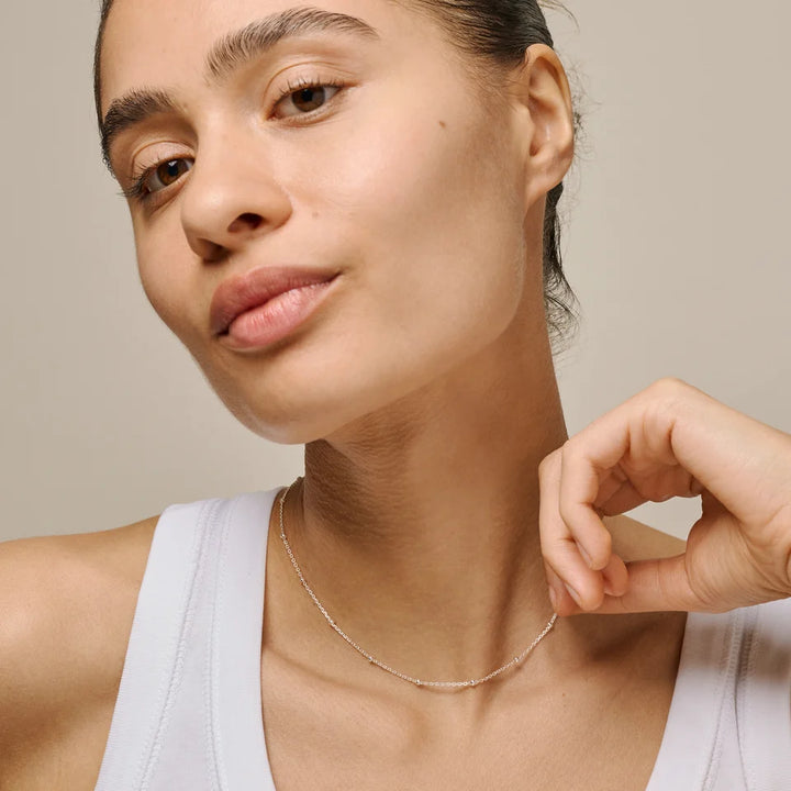 Woman wearing a delicate necklace against a neutral background