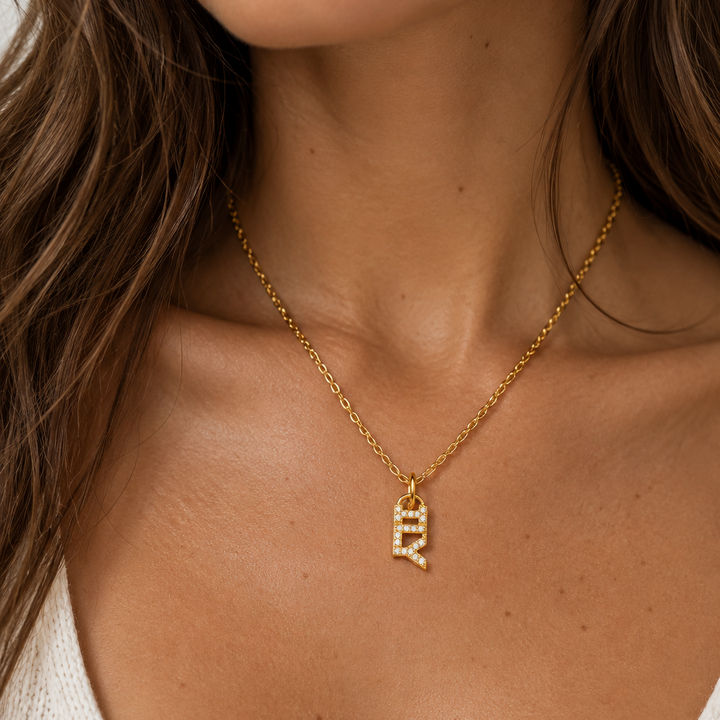 A close-up of a woman wearing a delicate gold chain necklace with a small ILY pendant studded with tiny clear stones.