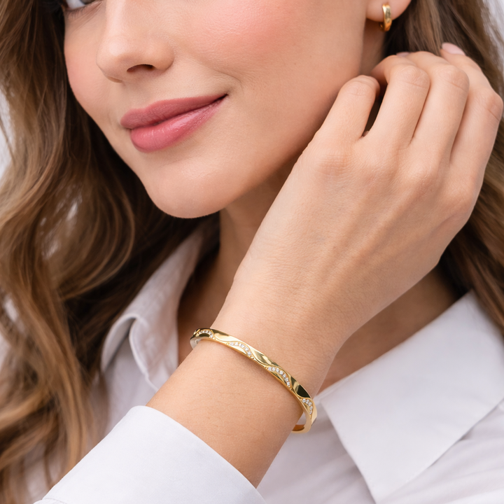 Woman wearing gold bracelet and earrings, close-up on face and hand.