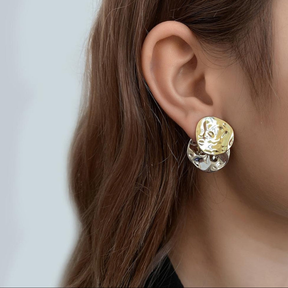 Close-up of an ear wearing a gold and silver earring against a neutral background