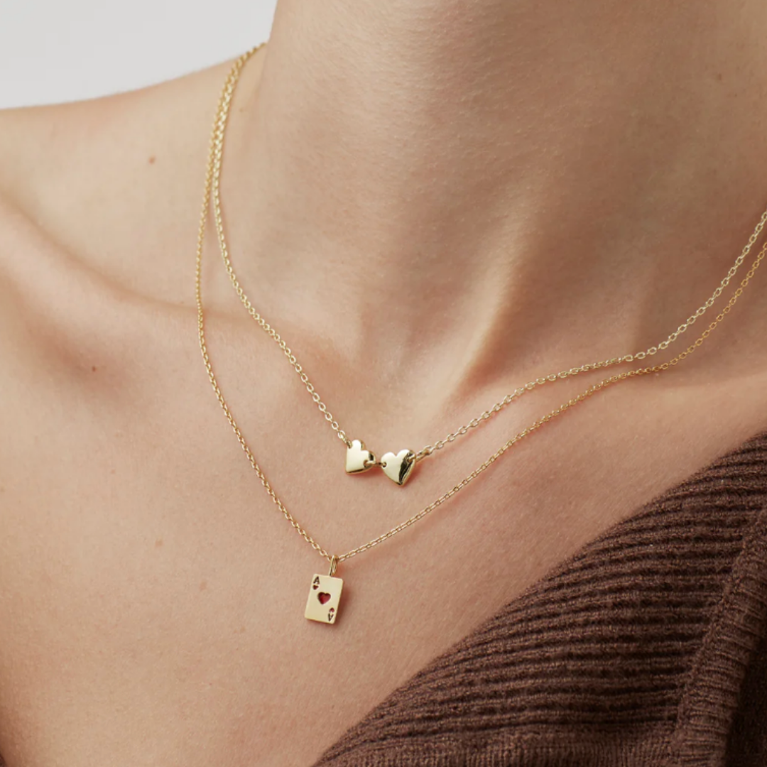 Gold necklace with heart pendants on a person wearing a brown top.