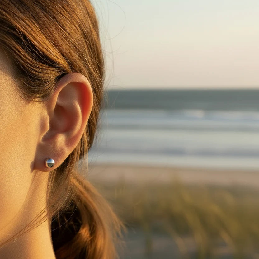 Close-up of a person's ear with an earring, blurred beach background