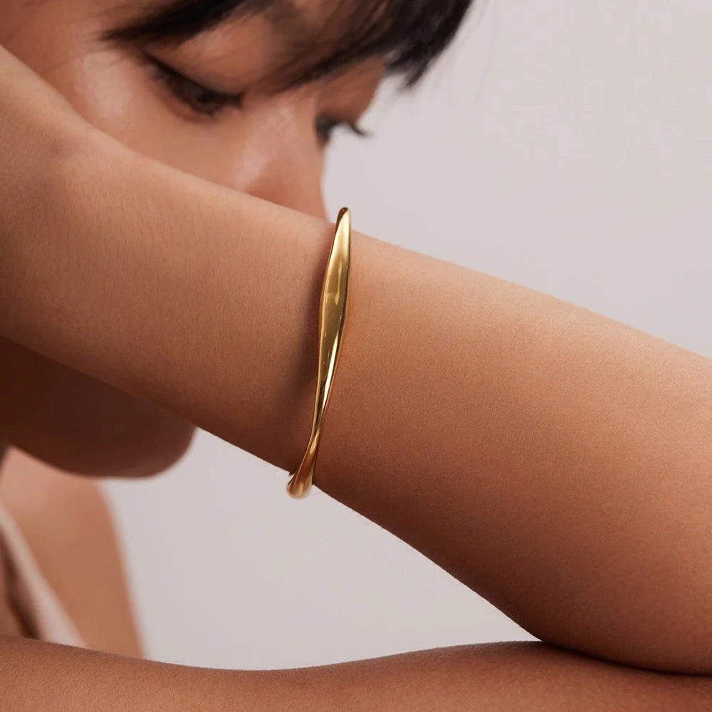 Gold bracelet on a person's wrist against a neutral background