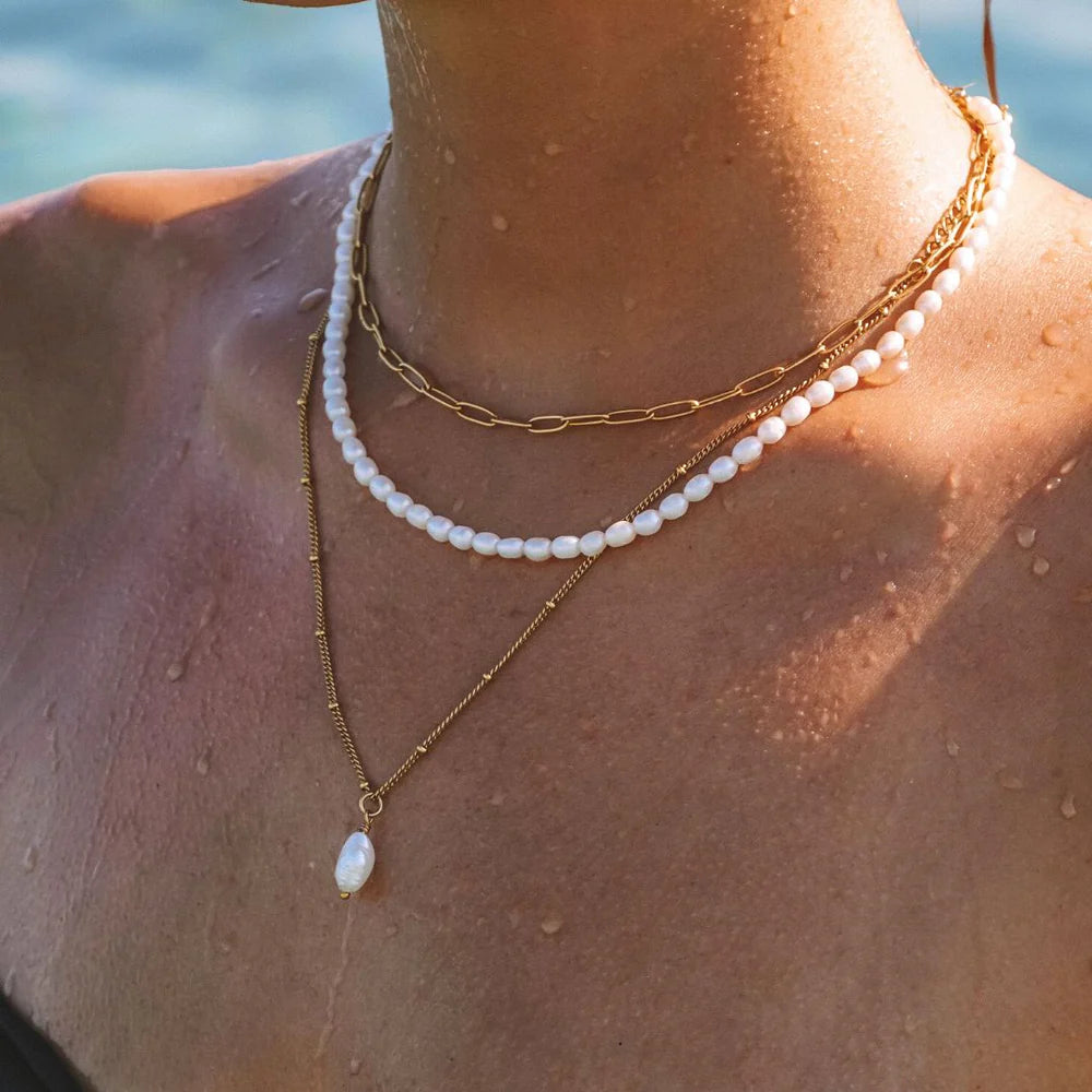 Close-up of a person wearing pearl and gold necklaces with a blurred natural background