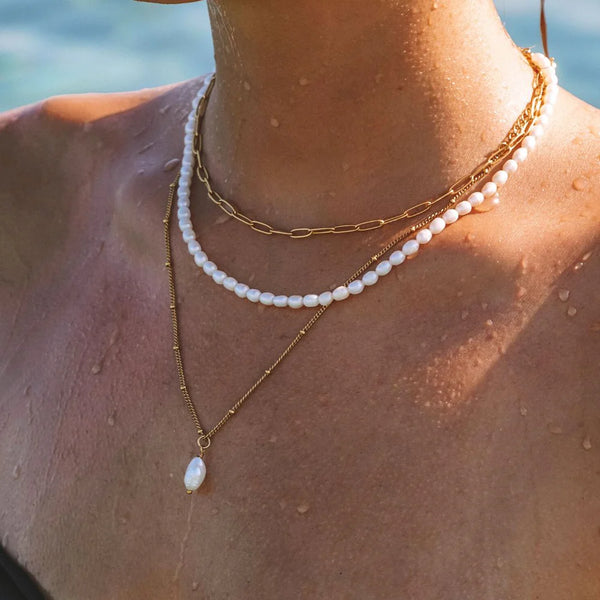 Close-up of a person wearing pearl and gold necklaces with a blurred natural background