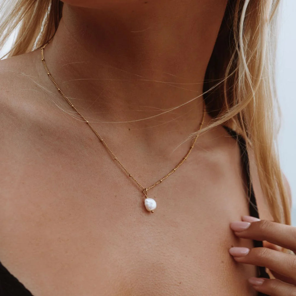 Gold necklace with a pearl pendant on a person's neck