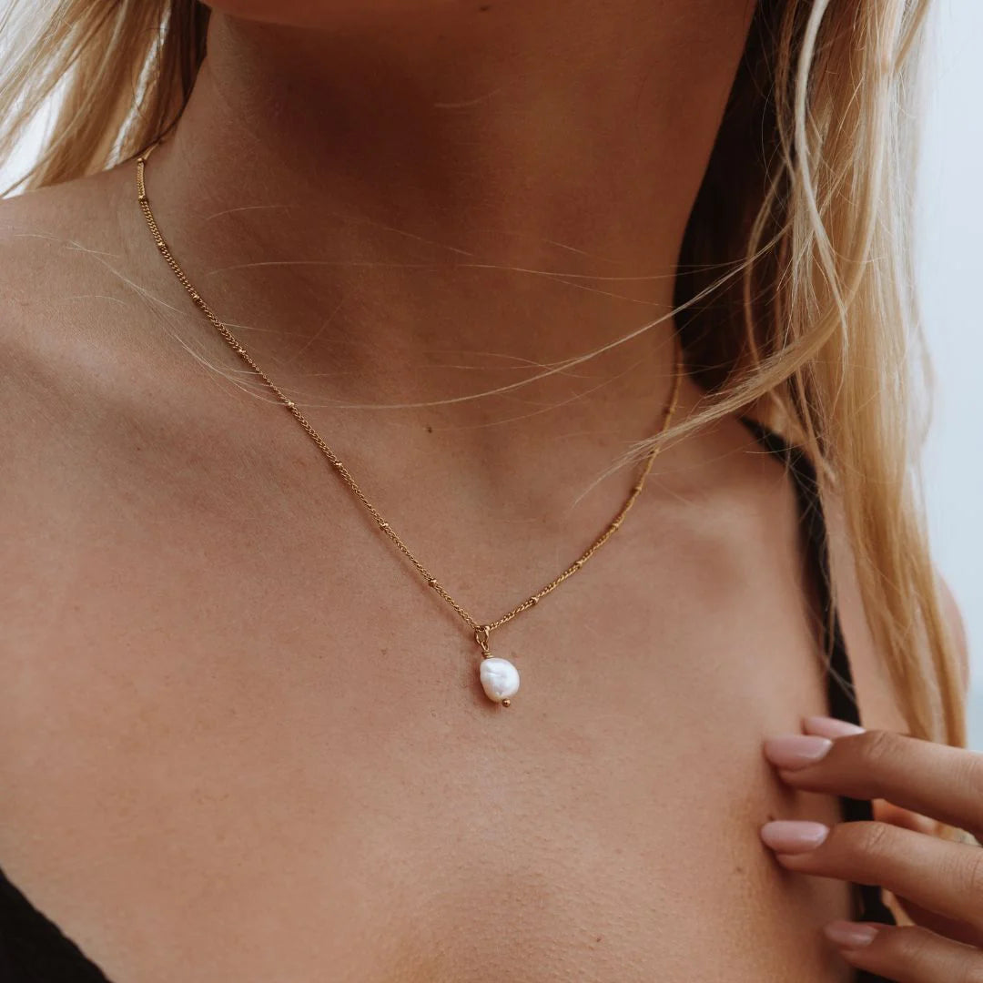 Gold necklace with a pearl pendant on a person's neck