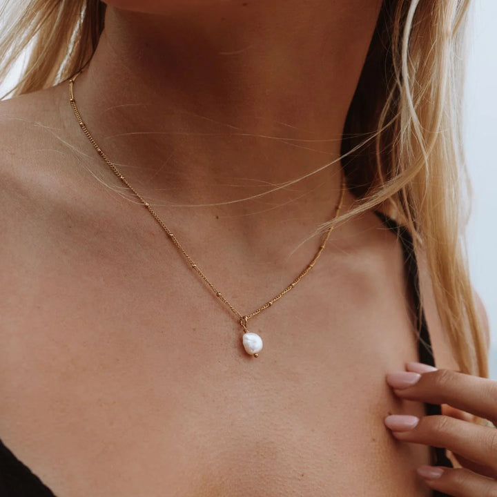Gold necklace with a pearl pendant on a person's neck