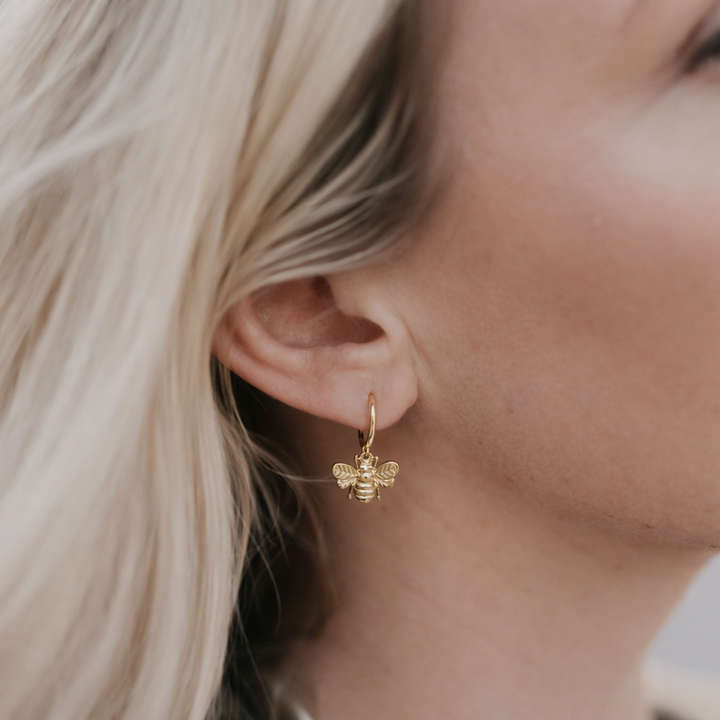 Gold bee-shaped earring worn by a person with blonde hair.