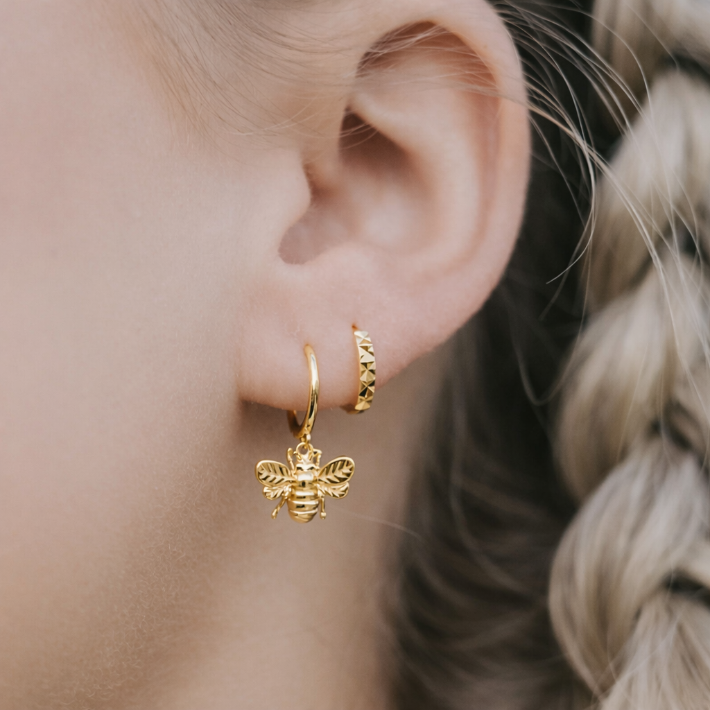 Gold bee-shaped earring worn by a person with blonde hair.