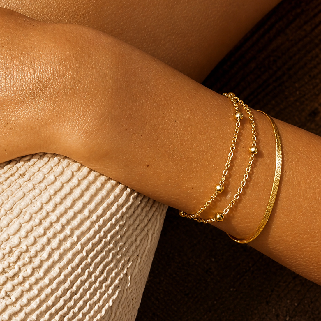 Close-up of a wrist wearing gold bracelets on a textured surface.