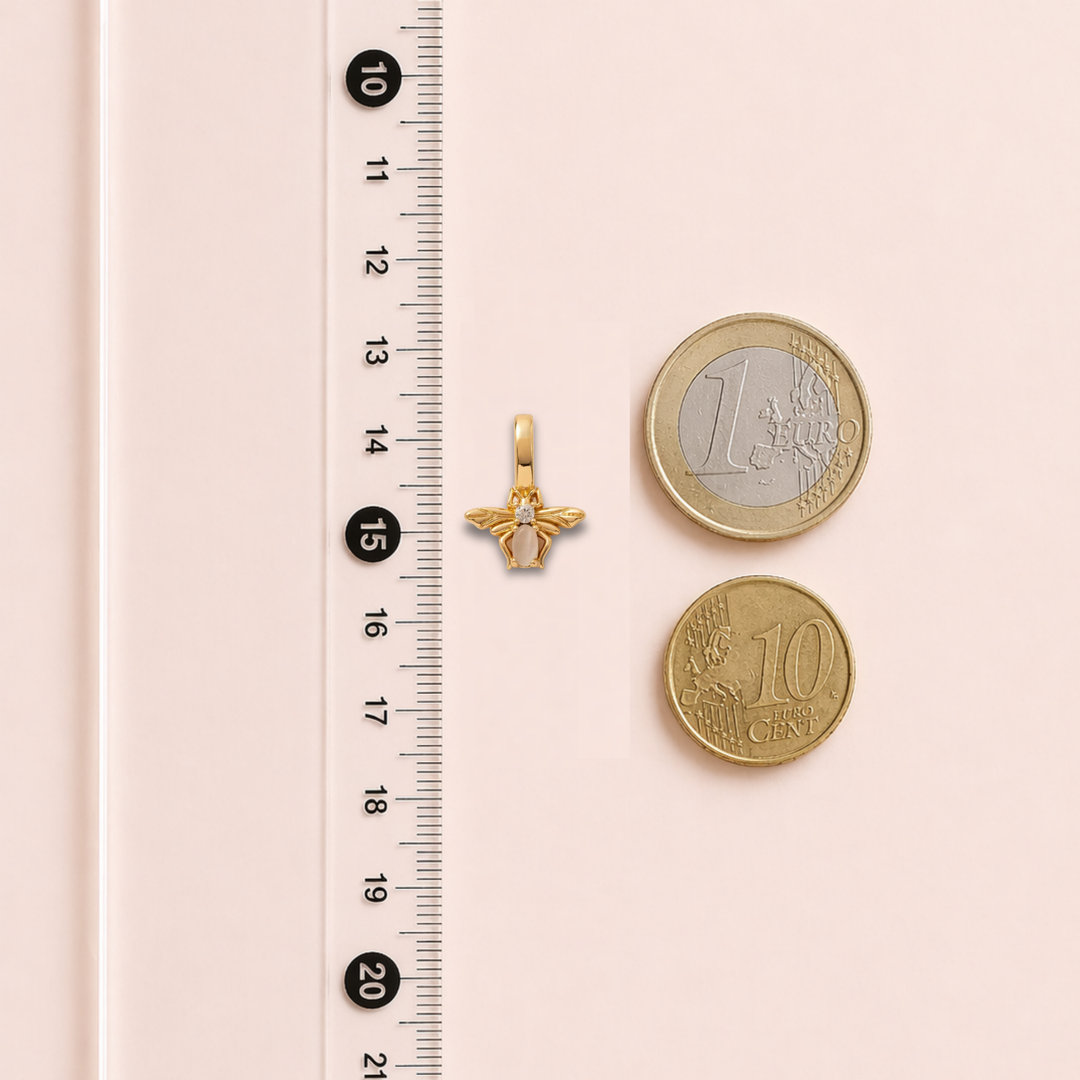 Gold pendant and two gold coins next to a ruler on a pink background