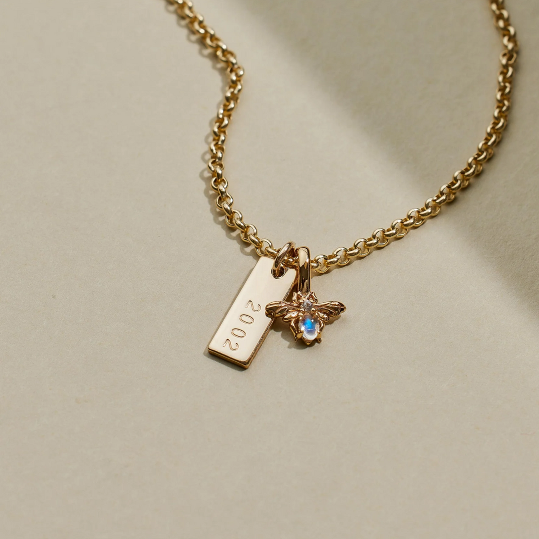 Gold necklace with a 'Bee Gemstone Charm' on a beige background