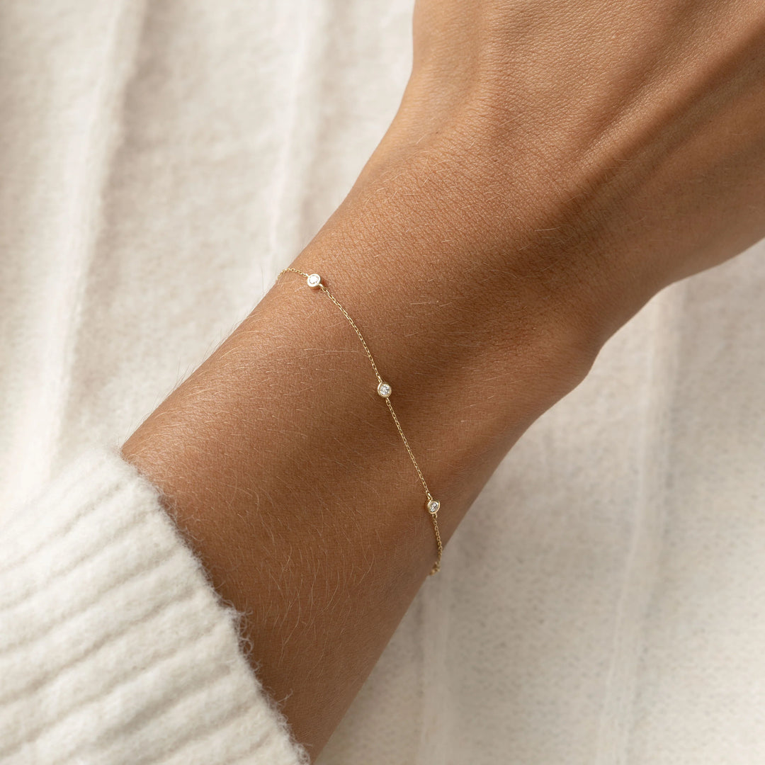 Gold bracelet with small beads on a wrist against a neutral background