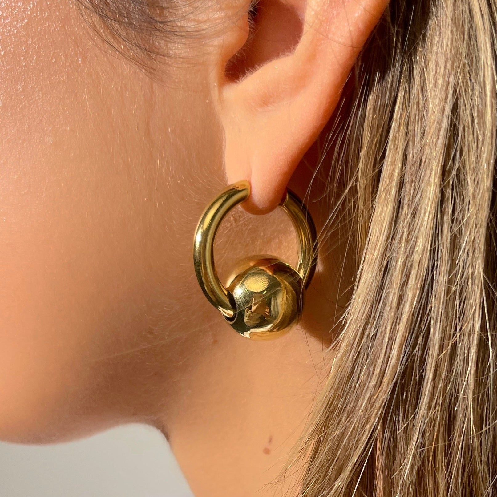 Gold hoop earring worn by a person with a neutral background
