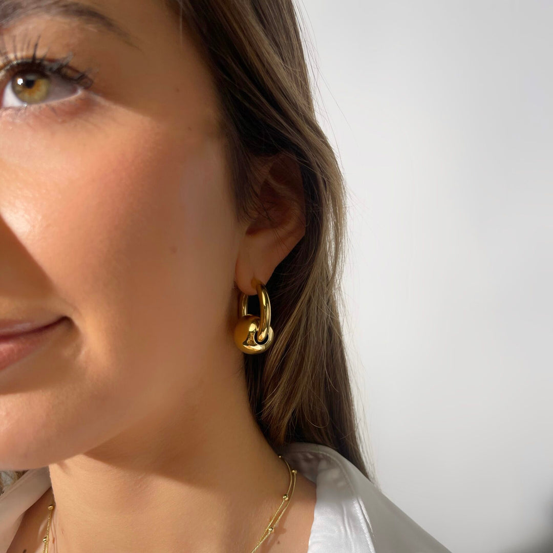 Close-up of a woman wearing gold hoop earrings and a white shirt.