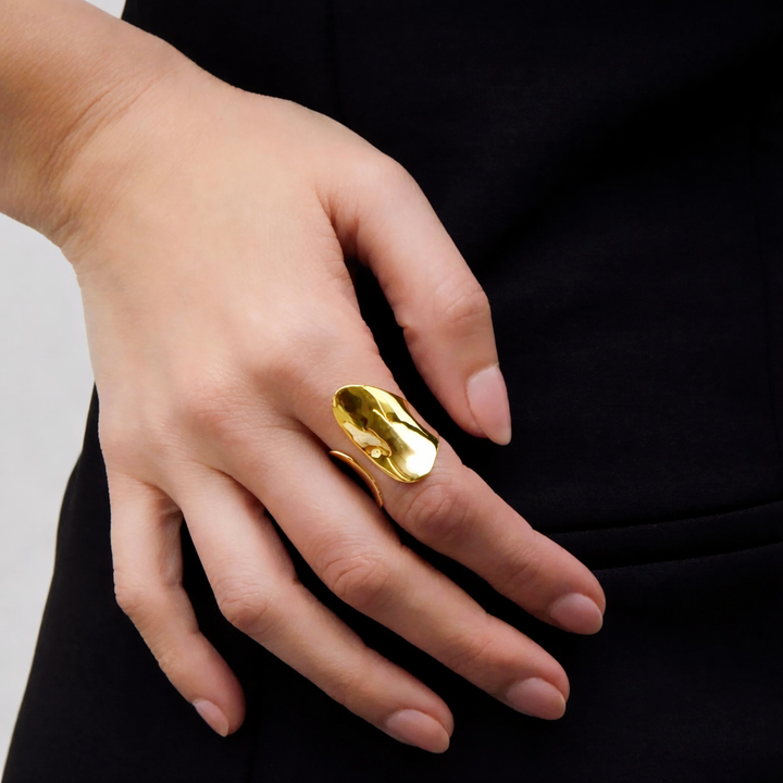 Hand wearing a gold ring with a plain background