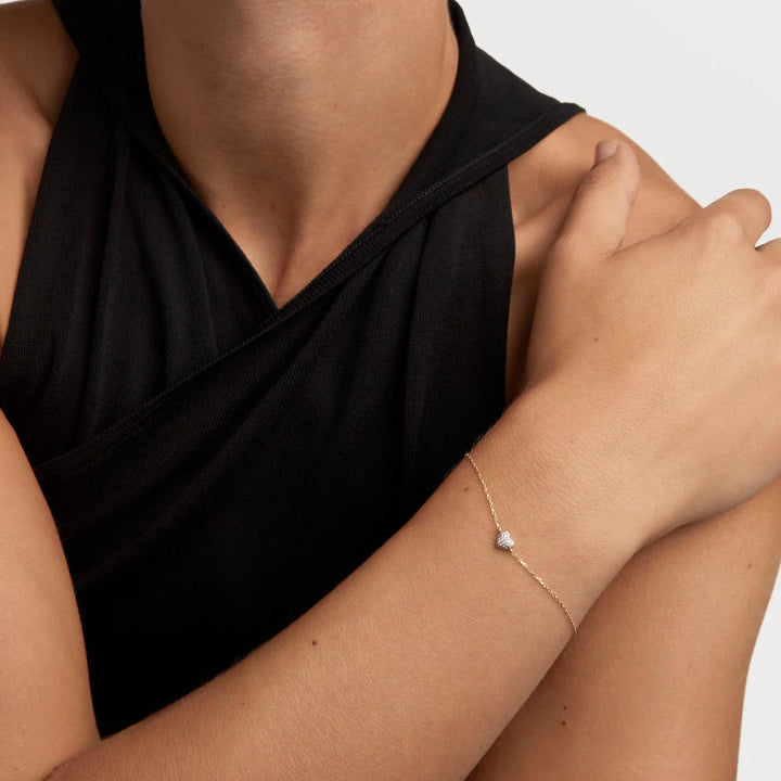 Person wearing a black sleeveless top with a gold bracelet on a white background