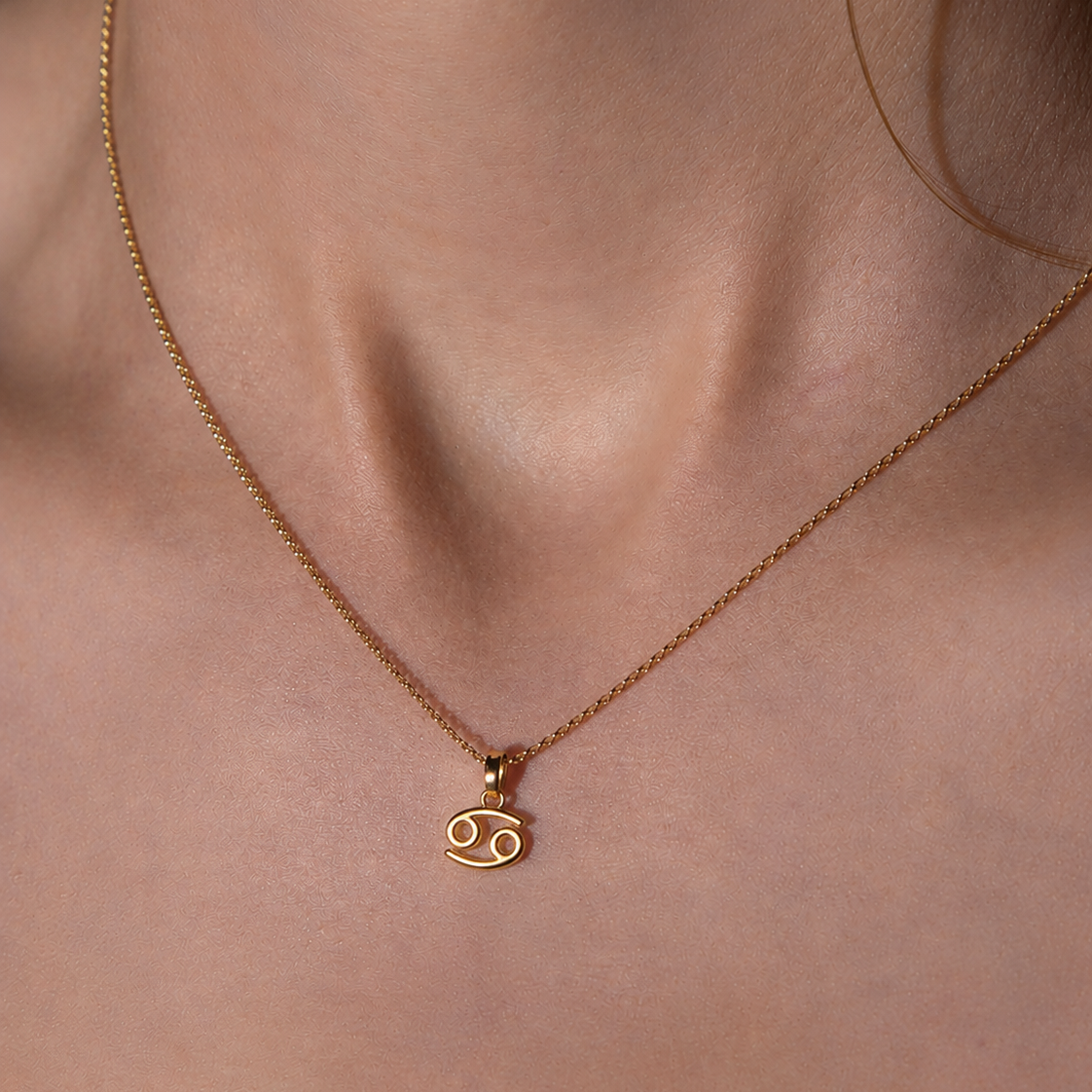 Gold necklace with a Cancer zodiac symbol pendant on a person's neck.