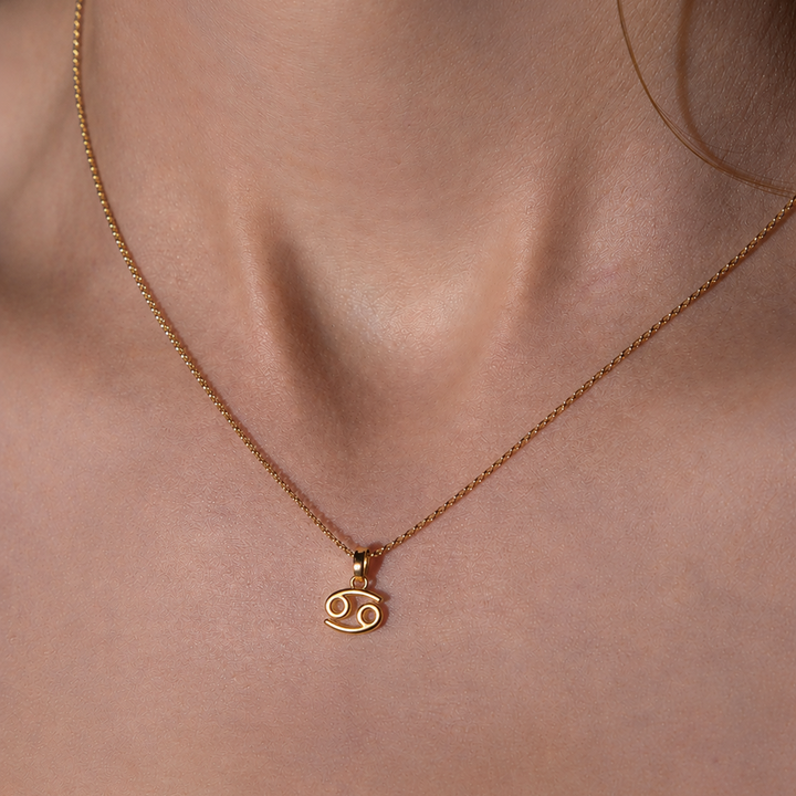 Gold necklace with a Cancer zodiac symbol pendant on a person's neck.