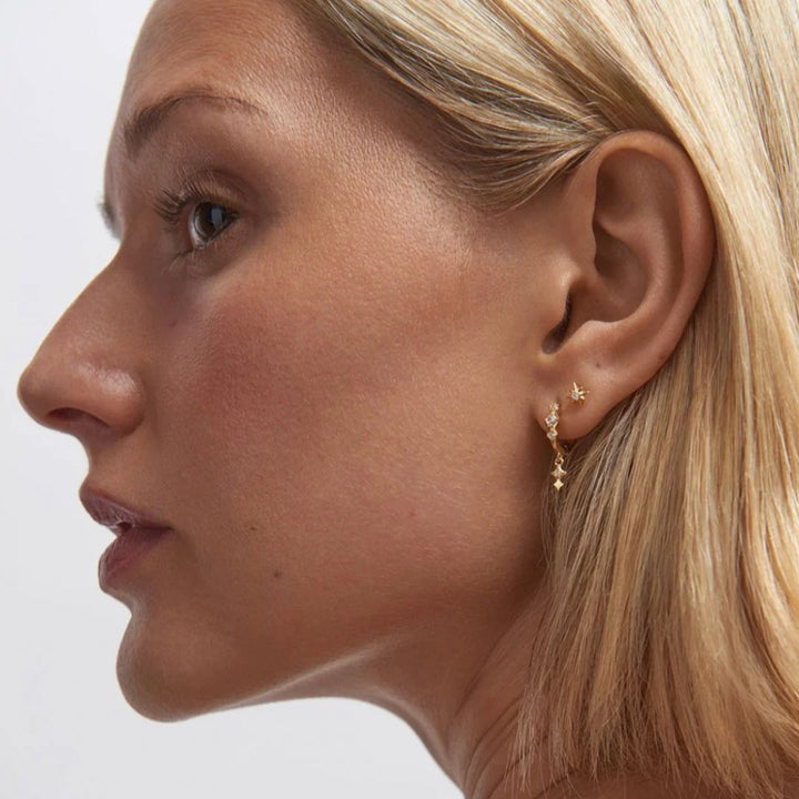 Close-up of a woman wearing gold earrings with a plain background
