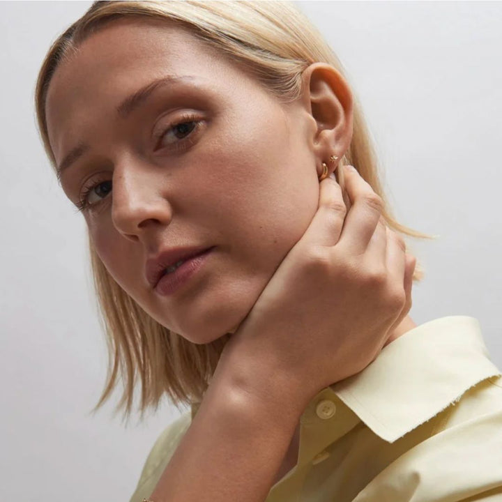 Woman adjusting an earring against a plain background