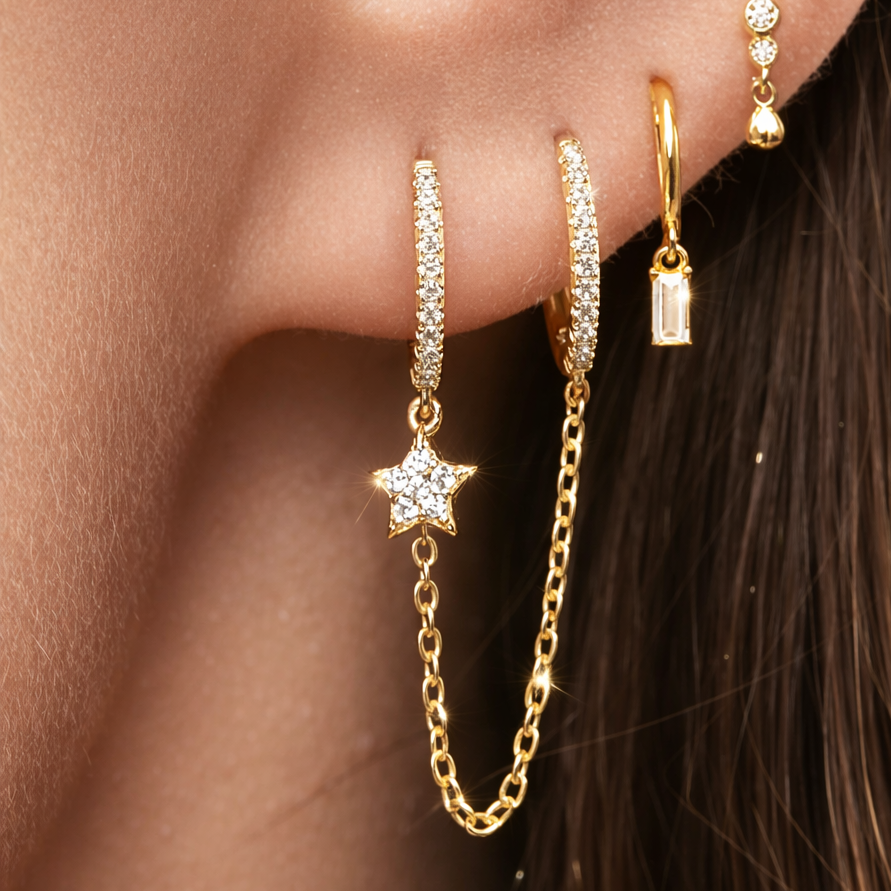 Close-up of a person wearing gold hoop earrings with star and chain details.