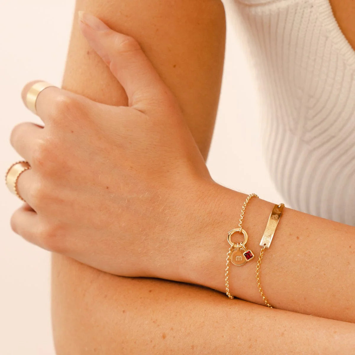 Close-up of a person's arm wearing gold jewelry on a neutral background
