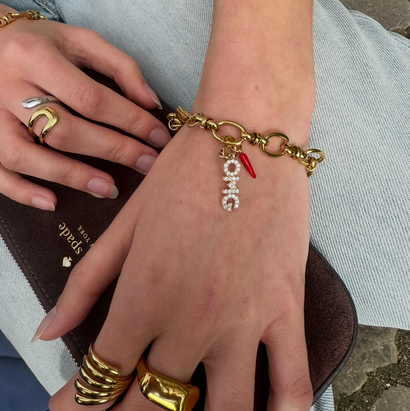 Close-up of a hand wearing a gold bracelet with charms, holding a brown clutch.