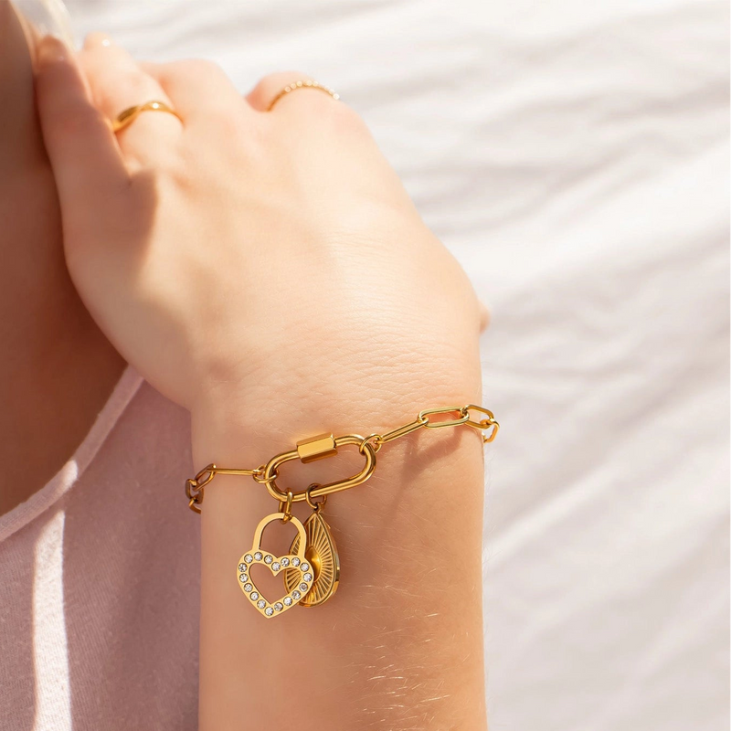 Gold bracelet with heart-shaped charms on a person's wrist against a light background