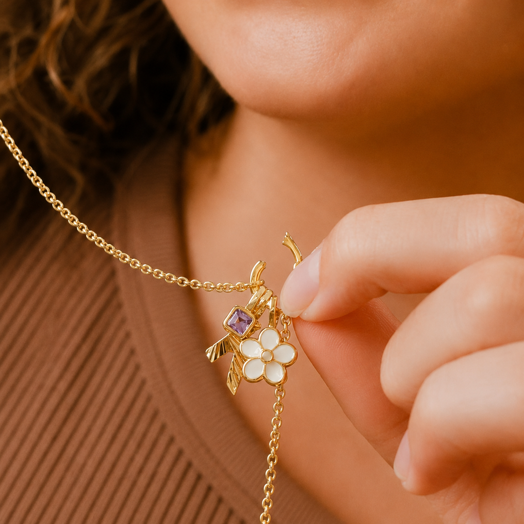 Close-up of a gold necklace with floral and purple gemstone pendant worn by a person.