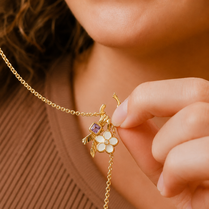 Close-up of a gold necklace with floral and purple gemstone pendant worn by a person.